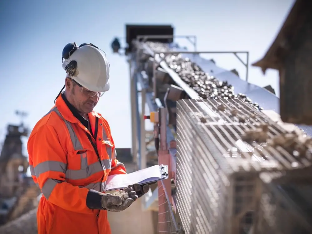 Worker inspecting stone conveyor belt and crushing machine in quarry 